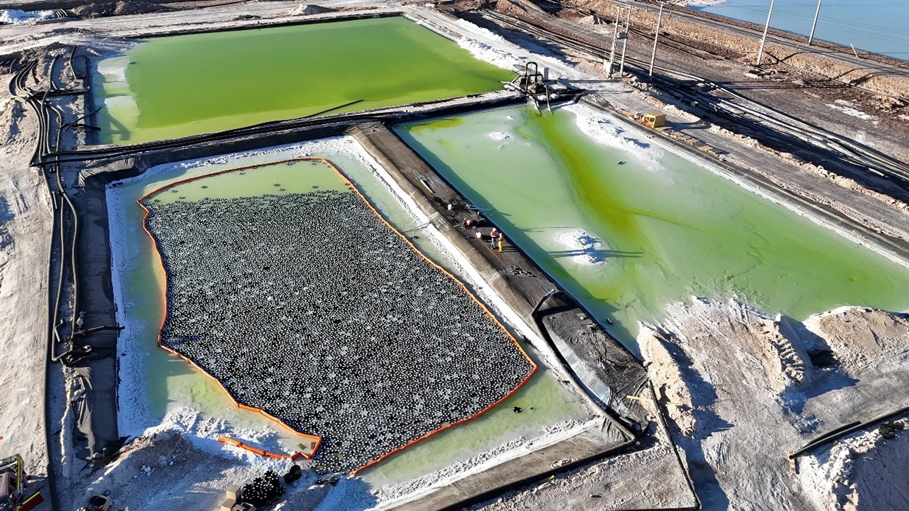Floating Lilypad modules cover part of an evaporation pond within an orange perimeter boom.